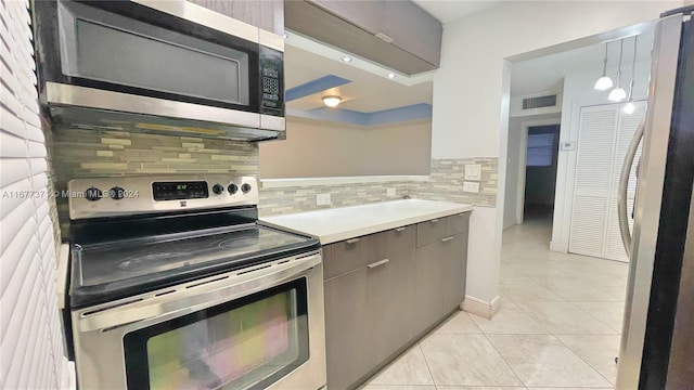 kitchen with appliances with stainless steel finishes, light tile patterned floors, decorative backsplash, and hanging light fixtures