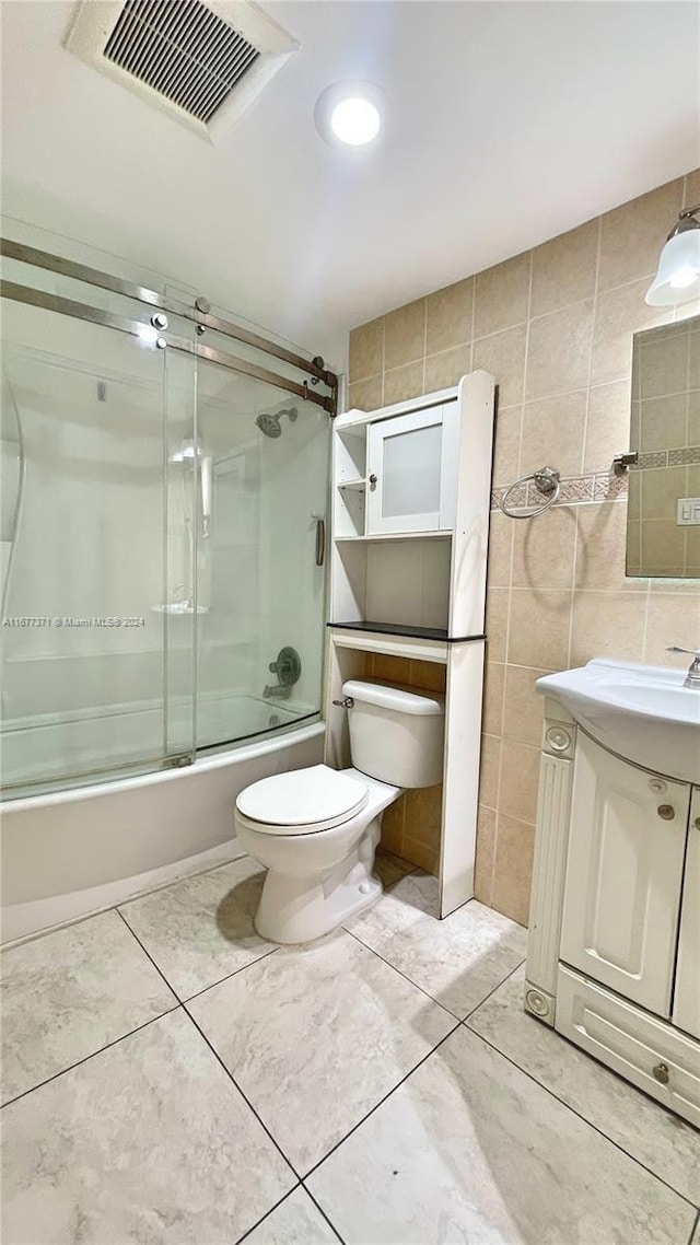 full bathroom featuring tile patterned floors, toilet, vanity, tile walls, and shower / bath combination with glass door