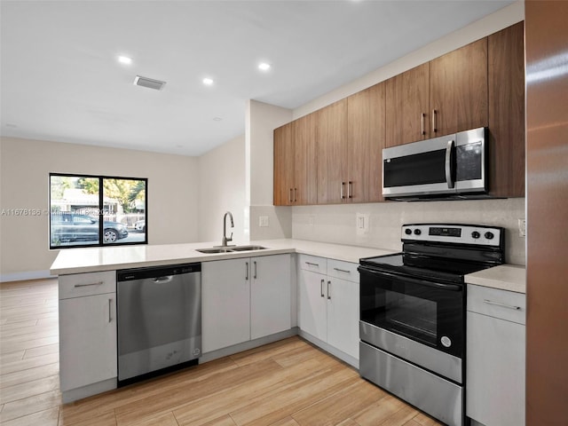 kitchen featuring kitchen peninsula, light wood-type flooring, stainless steel appliances, sink, and white cabinetry