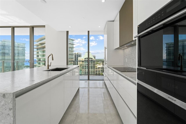 kitchen with floor to ceiling windows, modern cabinets, a sink, black appliances, and white cabinetry