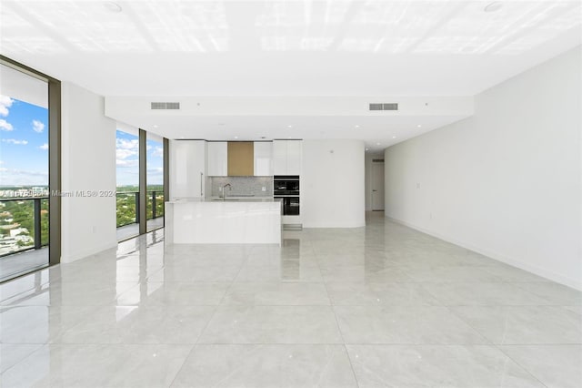 unfurnished living room featuring floor to ceiling windows, visible vents, baseboards, and a sink