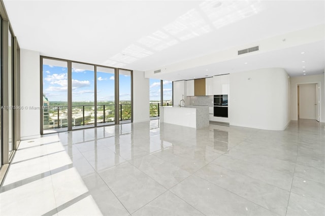 unfurnished living room featuring a sink, visible vents, and a wall of windows