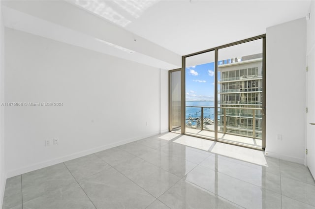 unfurnished room featuring baseboards, tile patterned flooring, a wall of windows, and a water view