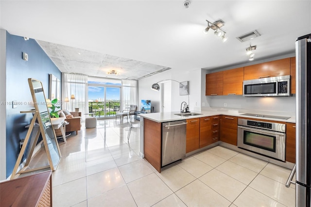 kitchen featuring sink, light tile patterned floors, appliances with stainless steel finishes, kitchen peninsula, and a wall of windows