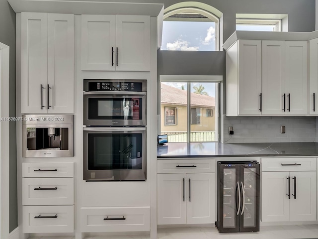 kitchen featuring decorative backsplash, white cabinets, wine cooler, and double oven