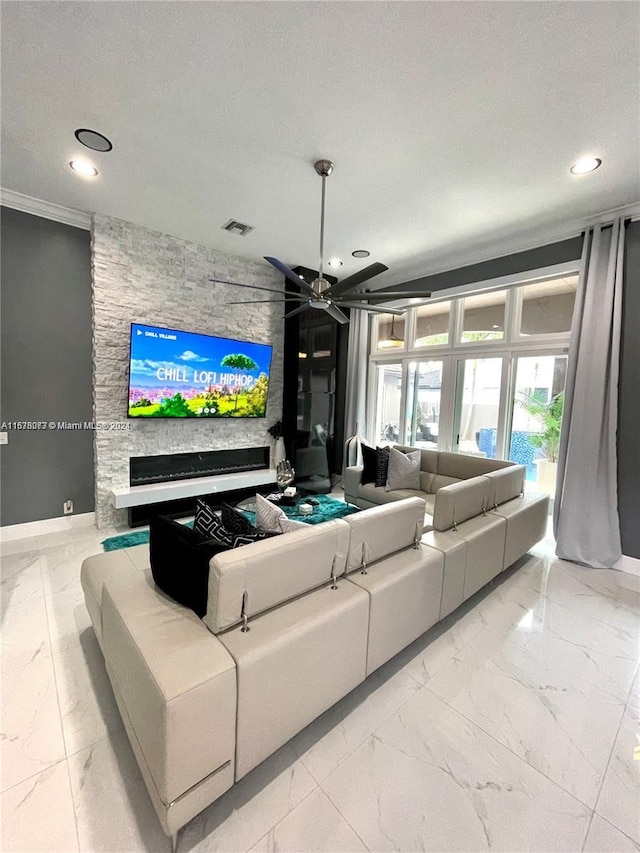 living room with ceiling fan, a stone fireplace, a textured ceiling, and ornamental molding