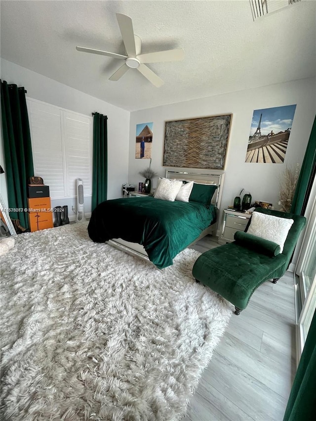 bedroom with a textured ceiling, light wood-type flooring, and ceiling fan