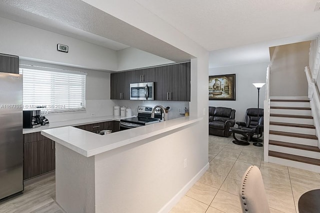 kitchen featuring appliances with stainless steel finishes, a textured ceiling, dark brown cabinets, kitchen peninsula, and light tile patterned floors