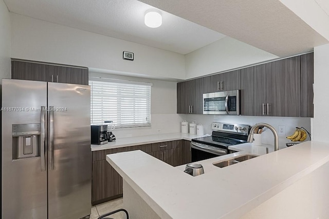 kitchen featuring appliances with stainless steel finishes, sink, a textured ceiling, kitchen peninsula, and light tile patterned floors