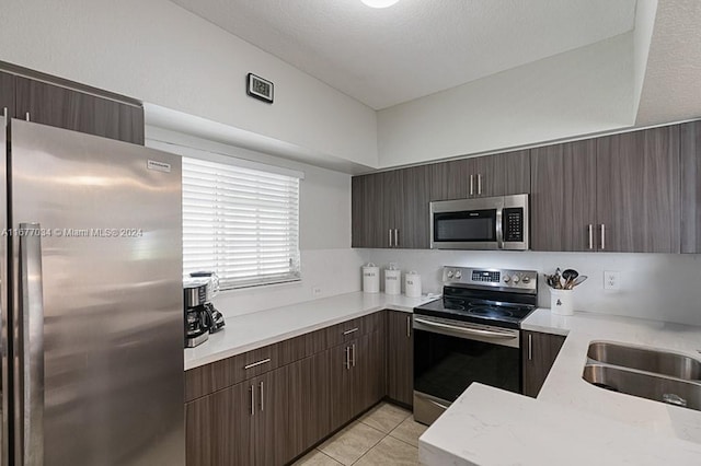 kitchen featuring sink, light tile patterned flooring, a textured ceiling, stainless steel appliances, and dark brown cabinetry