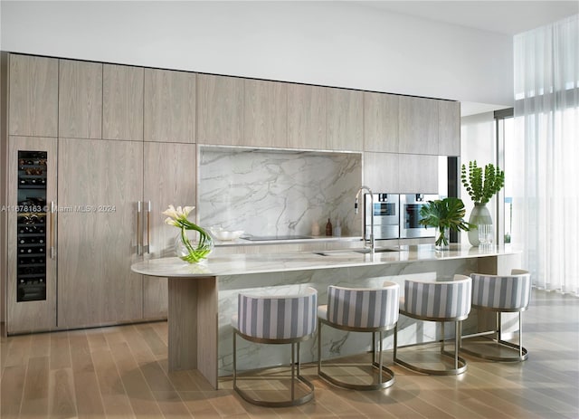 kitchen with light brown cabinets, tasteful backsplash, a breakfast bar, sink, and light stone counters