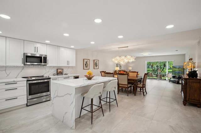 kitchen featuring a kitchen island, stainless steel appliances, light stone countertops, decorative light fixtures, and white cabinetry