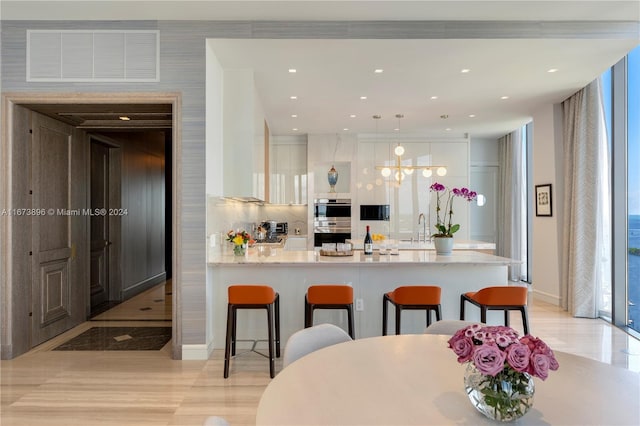 kitchen with a peninsula, a kitchen breakfast bar, stainless steel double oven, visible vents, and white cabinetry
