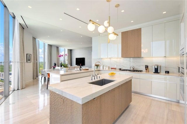 kitchen featuring stainless steel gas cooktop, modern cabinets, a sink, backsplash, and an island with sink