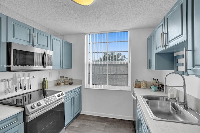 kitchen with appliances with stainless steel finishes, a textured ceiling, blue cabinets, and sink