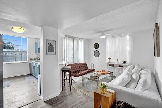 living room featuring ceiling fan, light hardwood / wood-style floors, a water view, and a textured ceiling