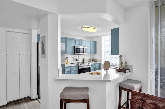 kitchen with kitchen peninsula, appliances with stainless steel finishes, blue cabinets, and a breakfast bar area