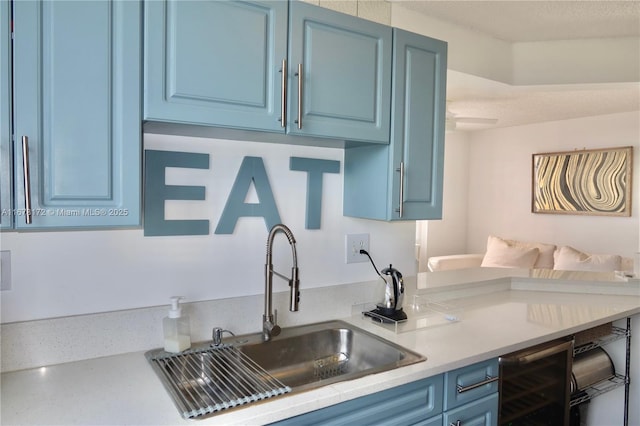 kitchen with a textured ceiling, blue cabinets, sink, and beverage cooler