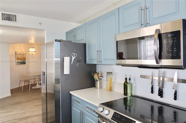 kitchen with appliances with stainless steel finishes, a textured ceiling, blue cabinets, light hardwood / wood-style floors, and hanging light fixtures