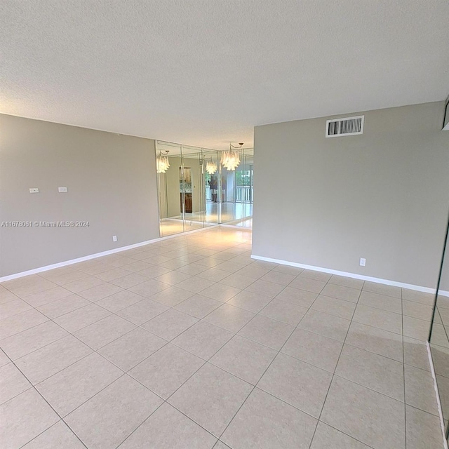 spare room featuring light tile patterned floors, a textured ceiling, and a notable chandelier