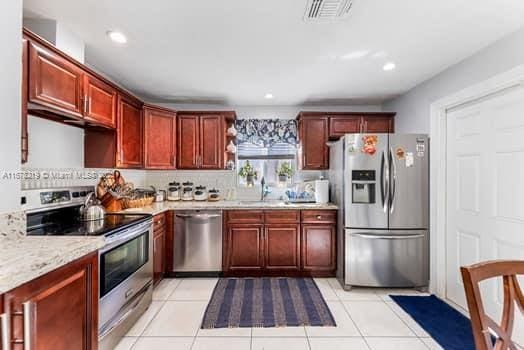 kitchen featuring light tile patterned flooring, appliances with stainless steel finishes, light stone counters, and sink