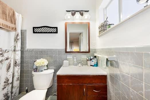 bathroom featuring a shower with shower curtain, vanity, toilet, and tile walls