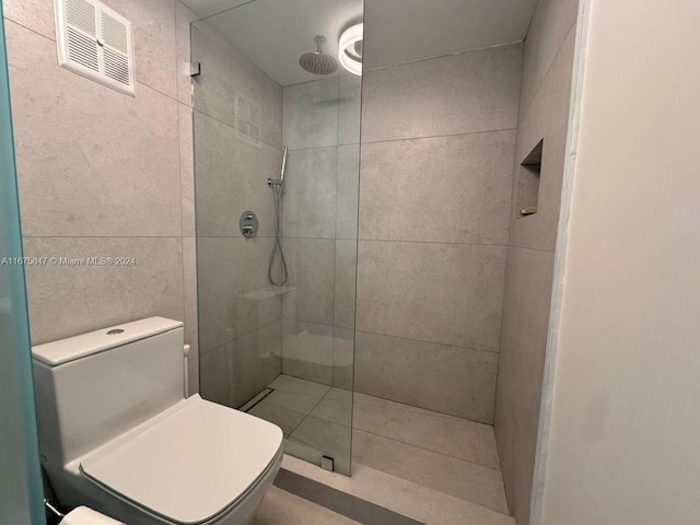 bathroom featuring tile walls, tiled shower, and toilet