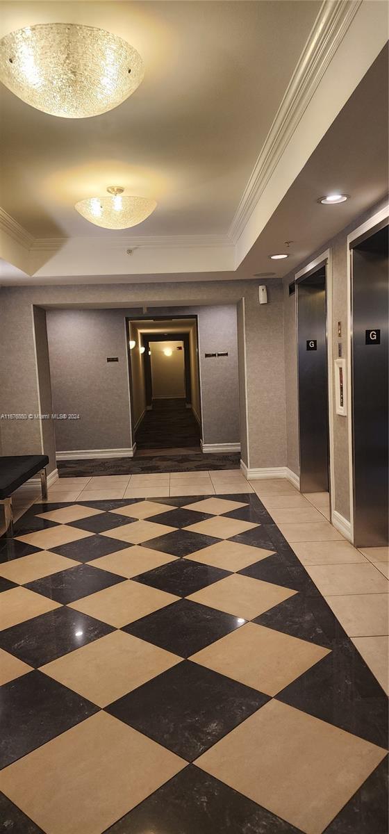 corridor with a tray ceiling, crown molding, and elevator