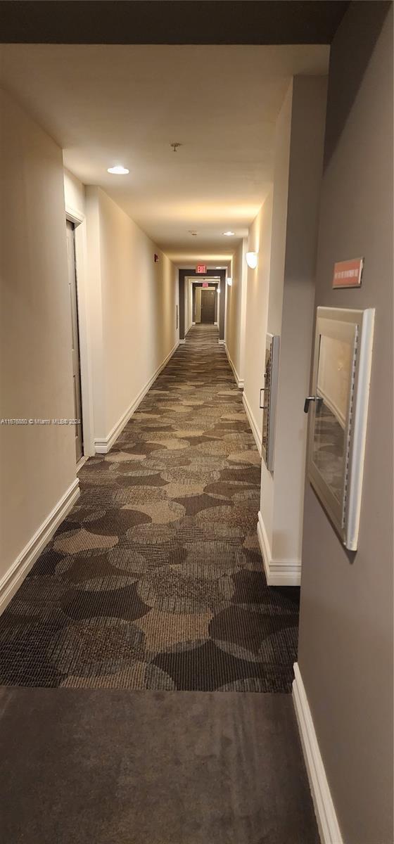 hall featuring dark colored carpet and baseboards