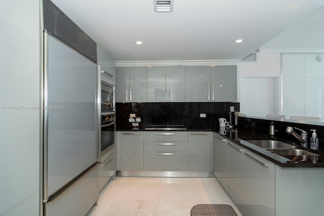 kitchen featuring built in appliances, dark stone counters, sink, light tile patterned floors, and tasteful backsplash