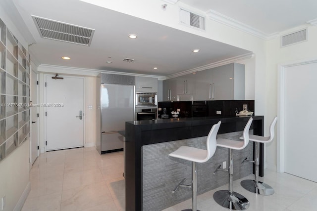 kitchen with built in appliances, a kitchen breakfast bar, crown molding, and gray cabinetry