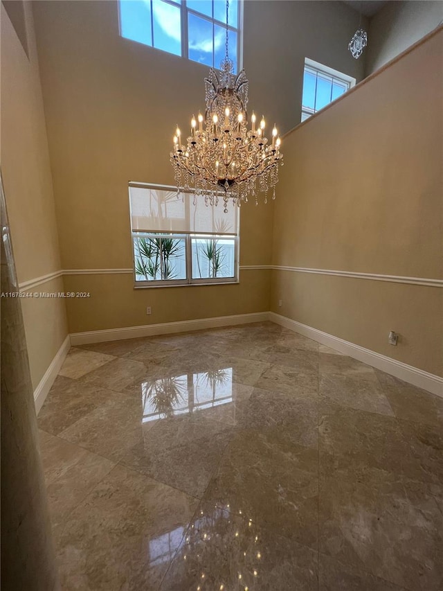 unfurnished dining area with a towering ceiling, an inviting chandelier, and a healthy amount of sunlight