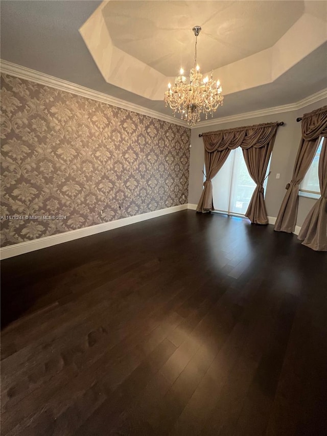 empty room with a raised ceiling, ornamental molding, a chandelier, and dark hardwood / wood-style floors