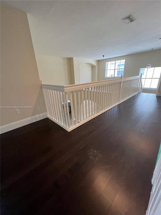 unfurnished room with a notable chandelier, a textured ceiling, and dark hardwood / wood-style flooring