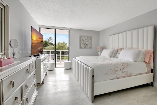 bedroom with access to exterior, a textured ceiling, light hardwood / wood-style floors, and floor to ceiling windows