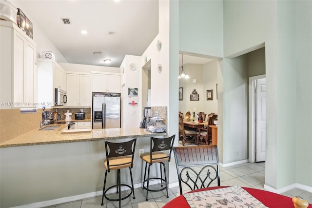 kitchen with light stone counters, backsplash, white cabinetry, appliances with stainless steel finishes, and light tile patterned flooring