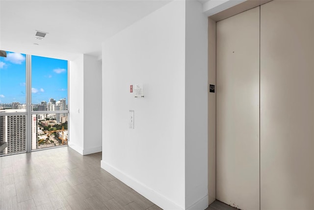 hall featuring floor to ceiling windows, wood-type flooring, and elevator