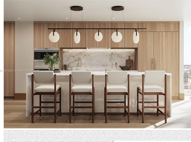 kitchen featuring a kitchen breakfast bar, hanging light fixtures, oven, and light wood-type flooring