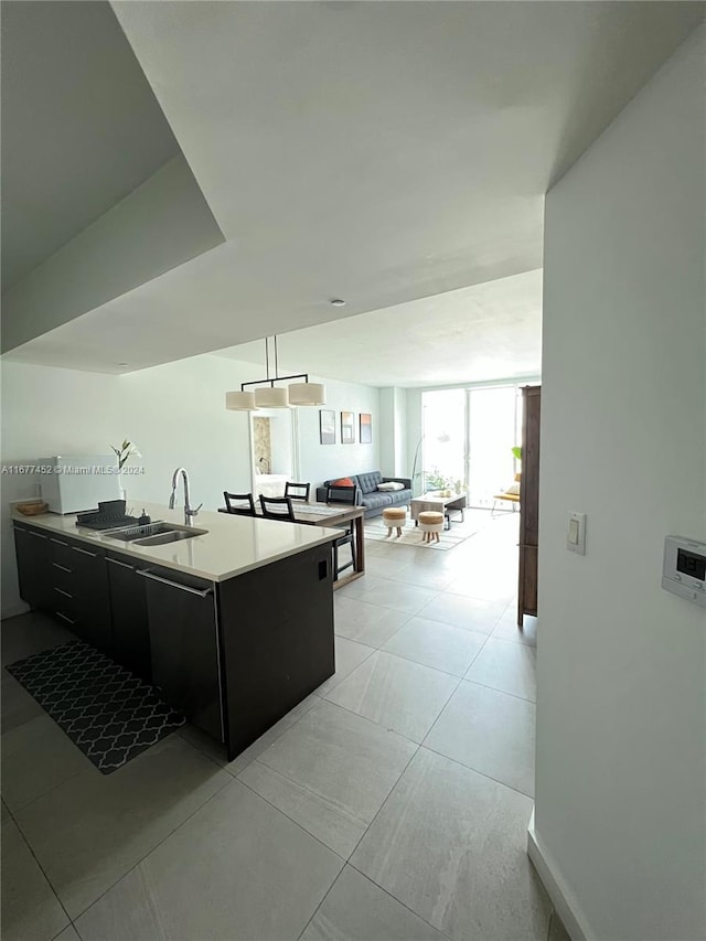 kitchen with light tile patterned flooring, open floor plan, light countertops, dark cabinetry, and a sink
