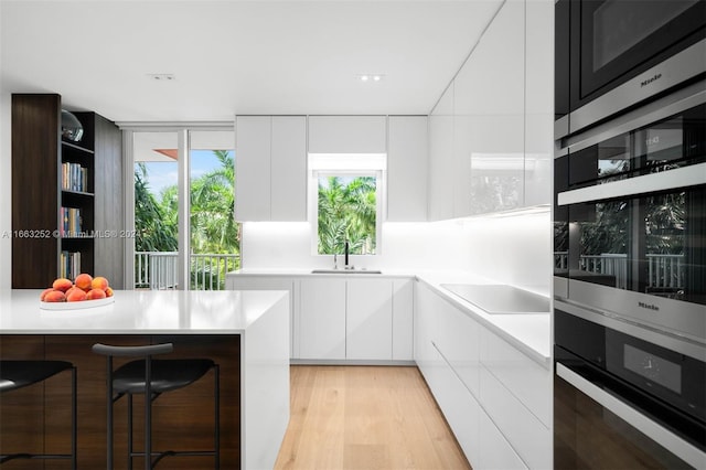 kitchen with sink, stainless steel oven, white cabinetry, and light hardwood / wood-style floors