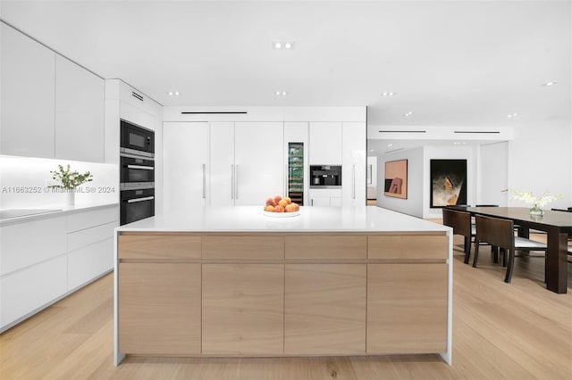 kitchen with a spacious island, white cabinets, stainless steel microwave, and light hardwood / wood-style floors