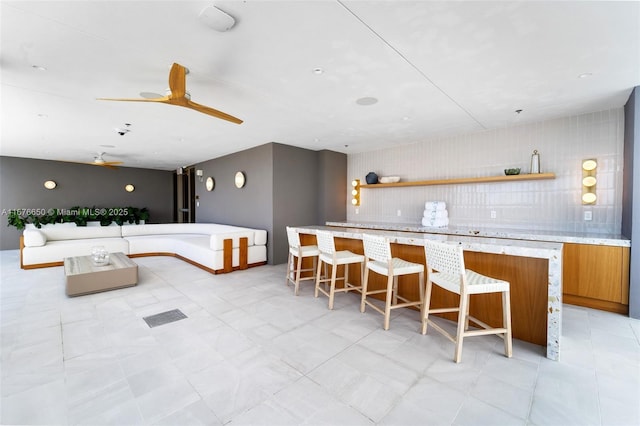 kitchen featuring tasteful backsplash, brown cabinets, a kitchen breakfast bar, a ceiling fan, and open shelves