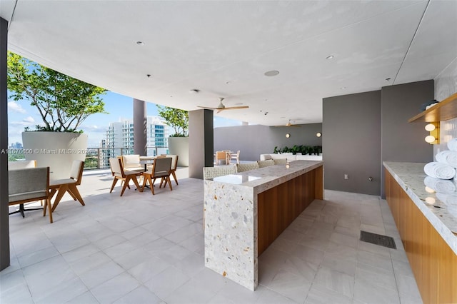 kitchen featuring ceiling fan, light stone countertops, light tile patterned floors, and a center island