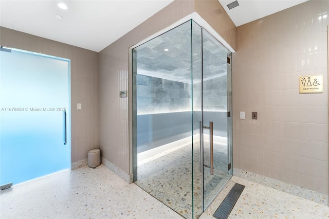 full bathroom with speckled floor, tile walls, a stall shower, and visible vents