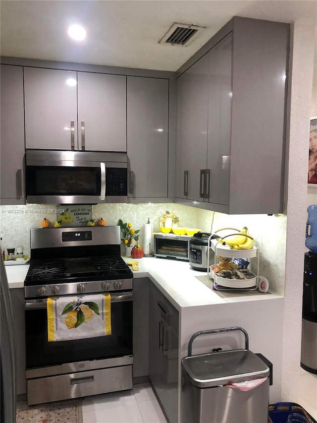 kitchen with gray cabinets, decorative backsplash, stainless steel appliances, and light tile patterned floors