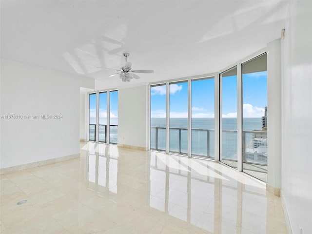 tiled empty room with expansive windows, a water view, and ceiling fan