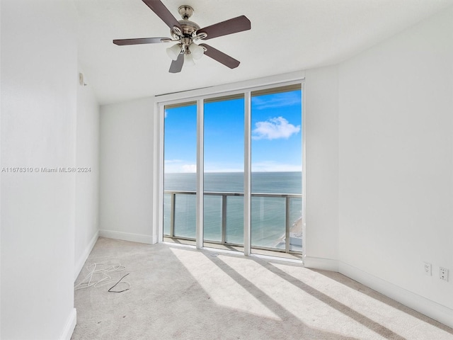 empty room with a water view, light carpet, a wall of windows, and ceiling fan