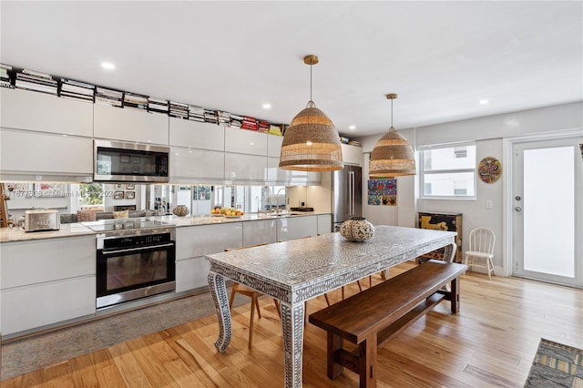 kitchen featuring plenty of natural light, pendant lighting, light wood-type flooring, white cabinetry, and appliances with stainless steel finishes