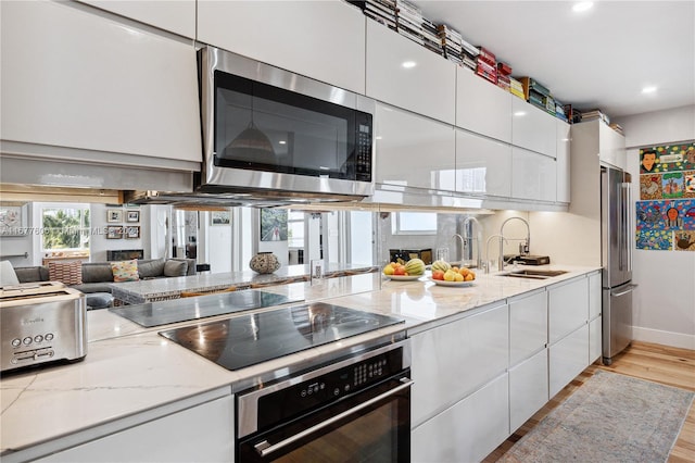 kitchen with appliances with stainless steel finishes, sink, light wood-type flooring, white cabinets, and light stone counters