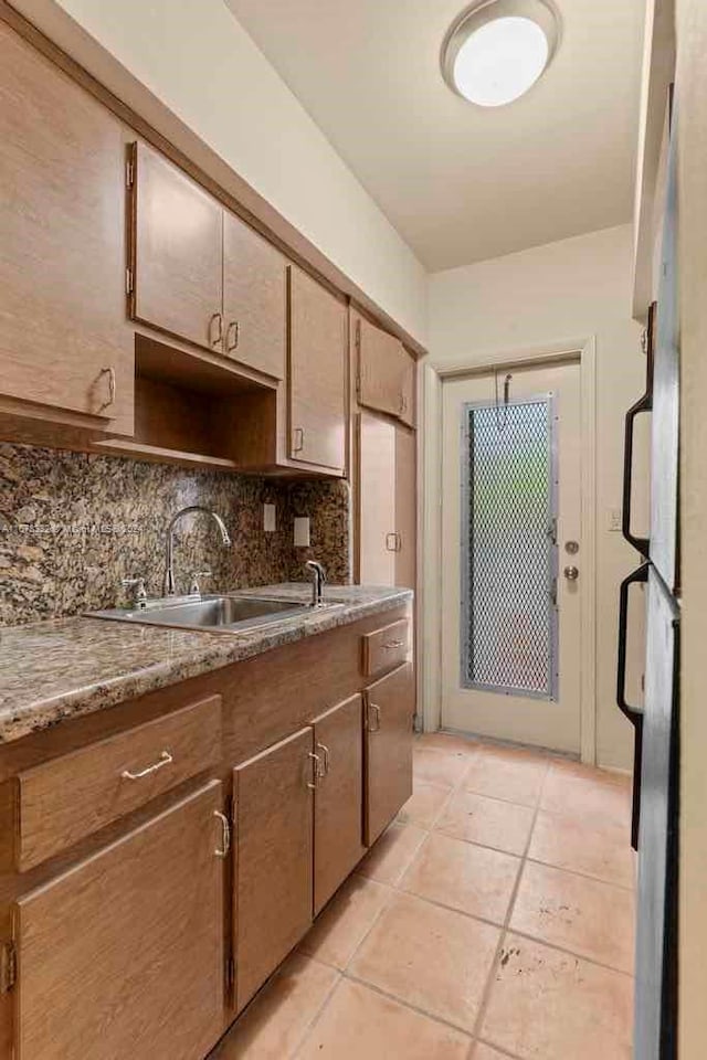 kitchen featuring freestanding refrigerator, light tile patterned flooring, decorative backsplash, and a sink